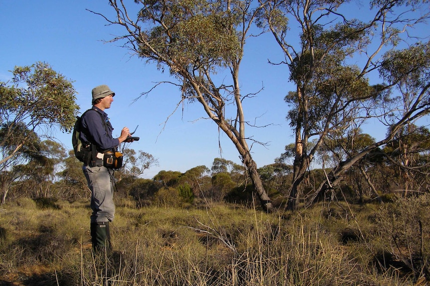 A man stands in the Australian outback holding equipment