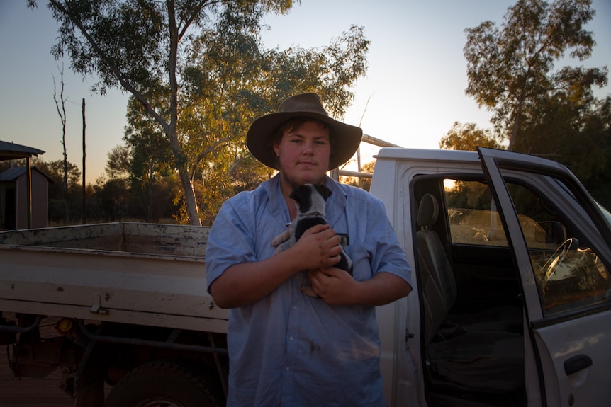 A young man holding a cattle dog pup near a ute