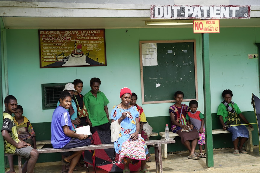 People sit on benches outside a building that is signed OUT-PATIENT. 