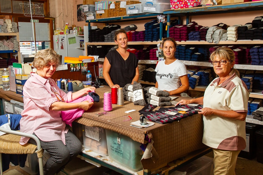 Four people posing around a workbench covered with woollen socks.