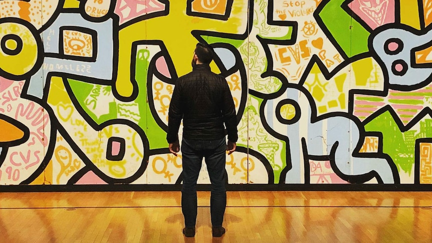 A man stands in front of a colourful graffiti-style artwork in the Chicago Cultural Centre.