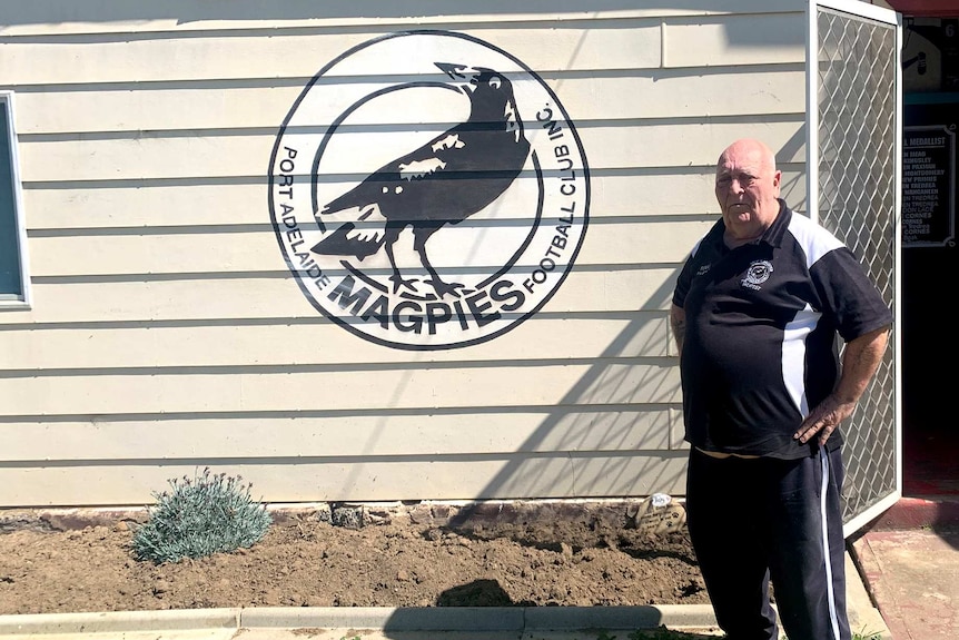 A man, wearing a black-and-white outfit, stands in front of a Magpies sign