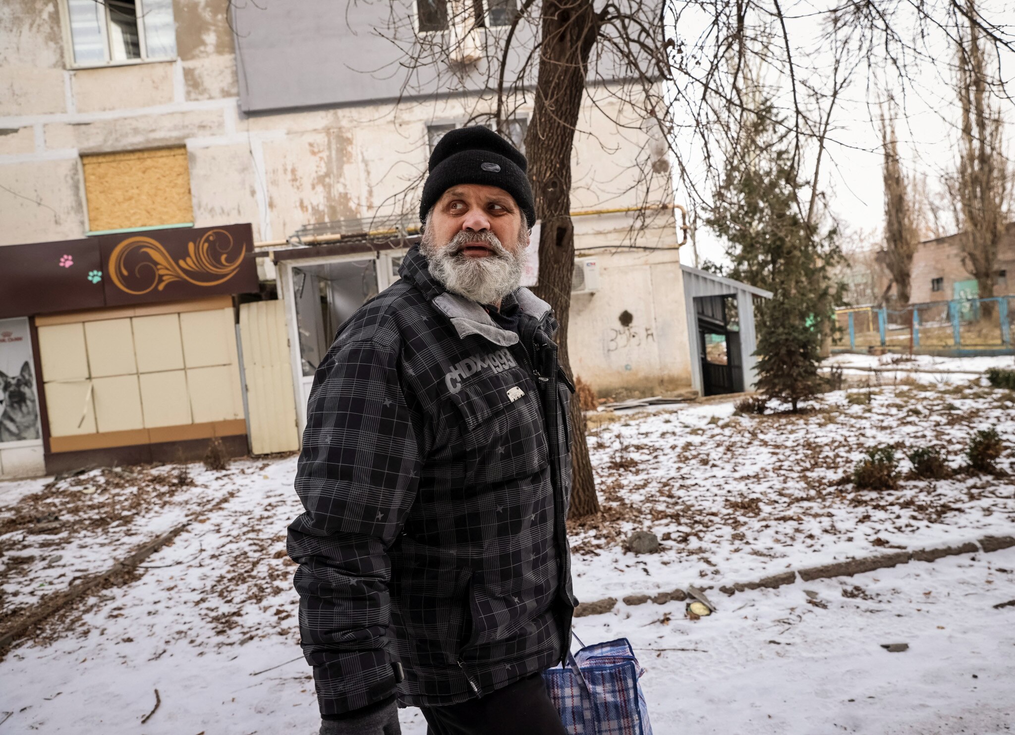 A local resident with a grey beard, wearing a beanie and a jacket, reacts during a shelling in Bakhmut