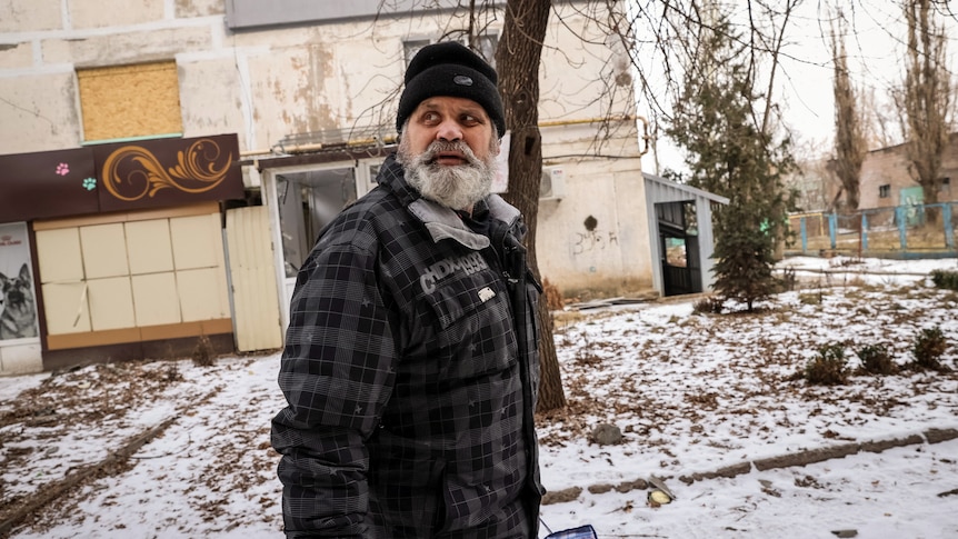 A local resident with a grey beard, wearing a beanie and a jacket, reacts during a shelling in Bakhmut