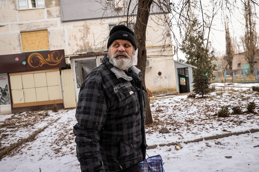 A local resident with a grey beard, wearing a beanie and a jacket, reacts during a shelling in Bakhmut