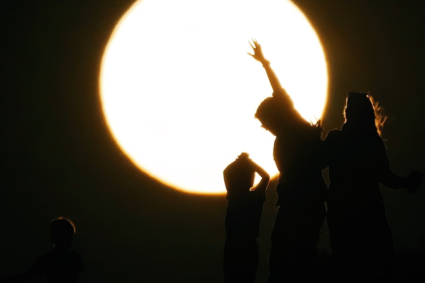 People in dancing in silhouette in front of the super blue moon.