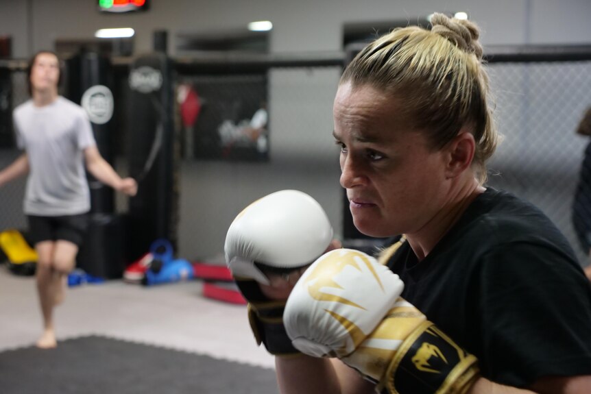 A woman punches a bag in a ring.