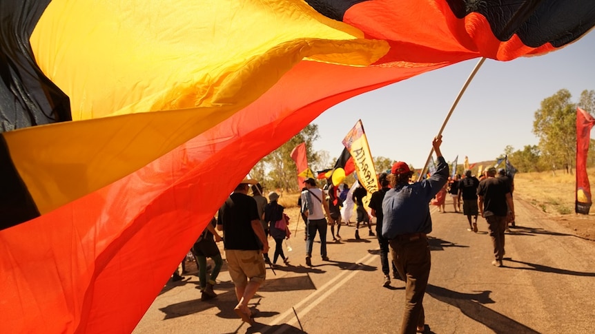 An Aboriginal flag is held by a man walking in the crowd