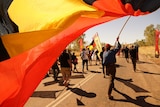 An Aboriginal flag is held by a man walking in the crowd