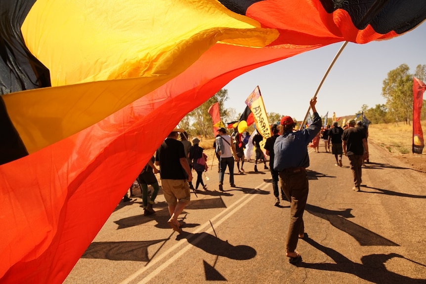 An Aboriginal flag is held by a man walking in the crowd