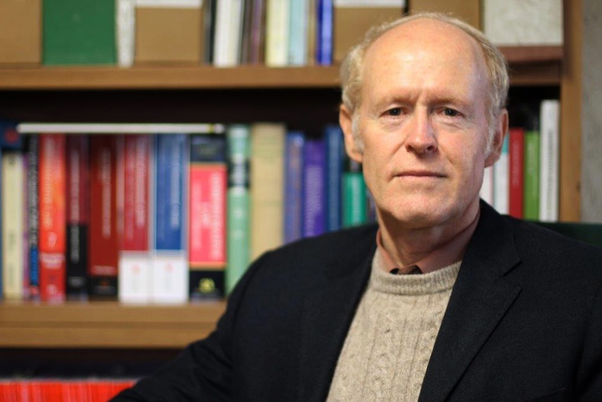 A head and shoulders shot of Alex Gardner sitting in front of a book case.