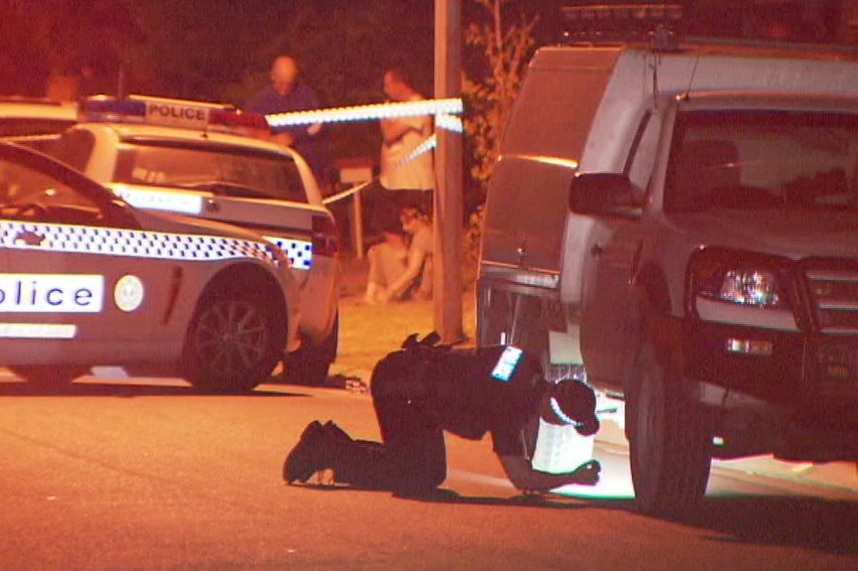 A police officer shines a torch under a ute at night