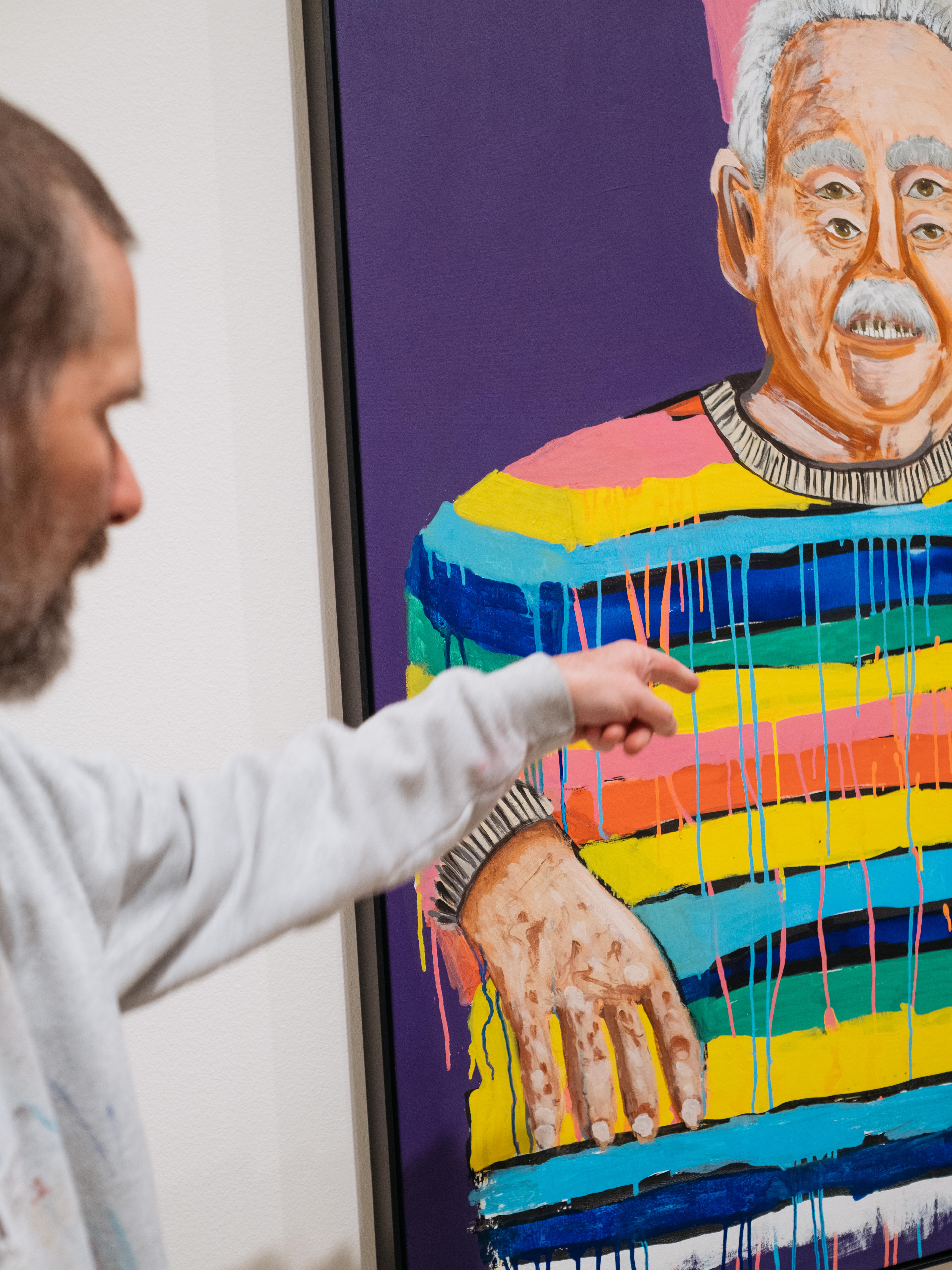 The artist blurred in the foreground points at a section of his vibrantly coloured poirtrait of Ken Done, in the gallery.