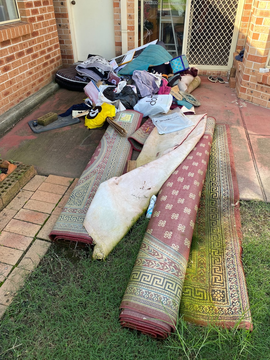 Rolled up carpets and personal belongings on the ground outside the house.