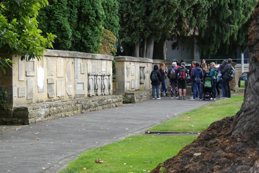 A tour guide leads a group of tourists through St David's Park, stopping to show them the grave headstone wall.