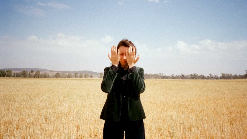 Gordi, standing in a wheat field, with her hands infront of her face