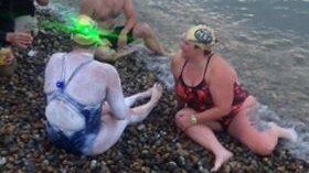 Sarah Thomas sitting on a pebble beach in her swimmers, a green light shining from her cap.