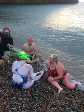 Sarah Thomas sitting on a pebble beach in her swimmers, a green light shining from her cap.