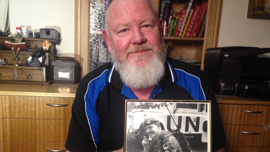 Mick Quinn holds a black and white photo of himself as a United Nations peacekeeper in Cambodia.