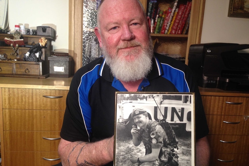 Mick Quinn holds a black and white photo of himself as a United Nations peacekeeper in Cambodia.