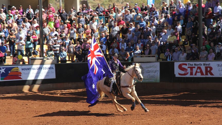 A lone horse rider in a rodeo arena holding a large Australian flag.