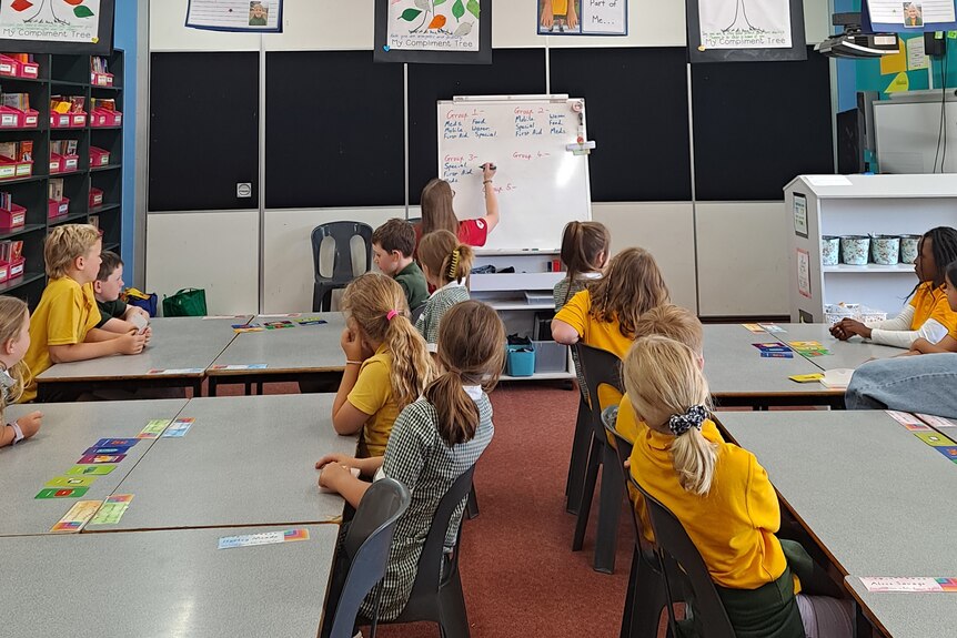 Grade three and four students face a white board where an Australian Red Cross representative is teaching 