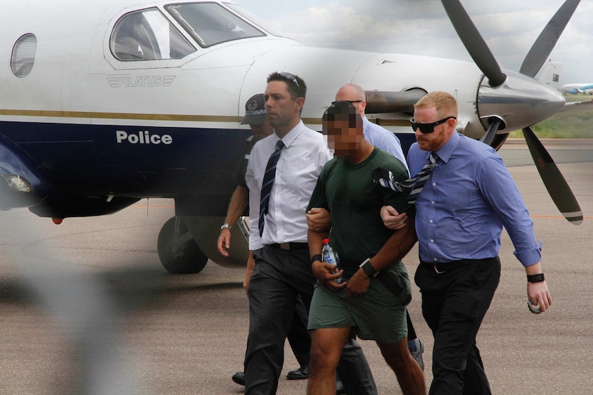 Jermaine Austral is escorted by police across the airfield in Alice Springs