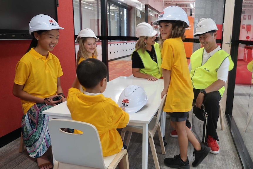 Students and their parents sit on tables and chairs in a meeting room