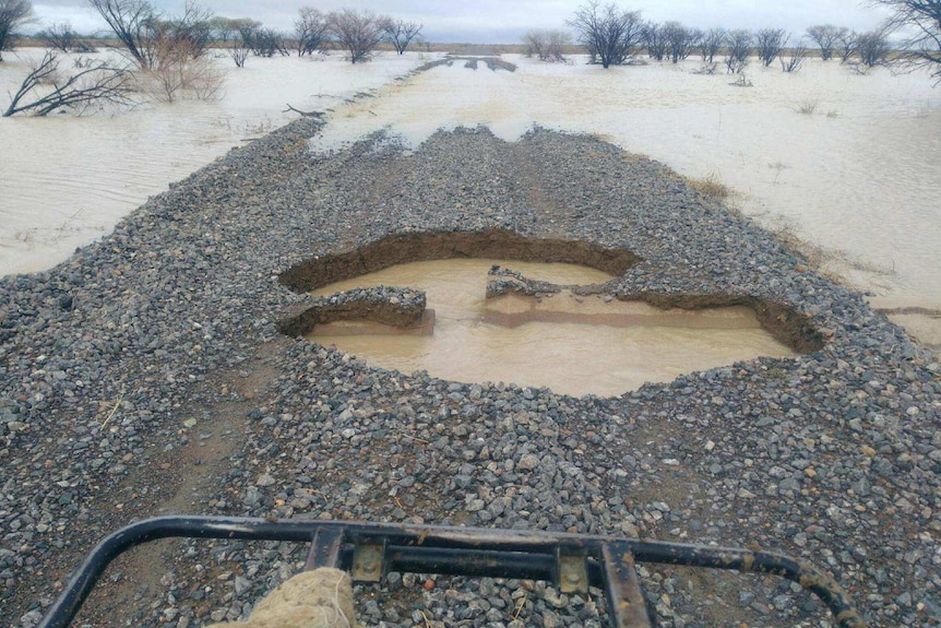A gravel road shows major potholes and either side is surrounded by water.