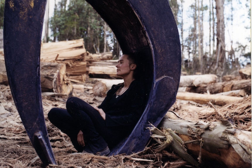 A young woman sits in the jaws of a piece of logging machinery.