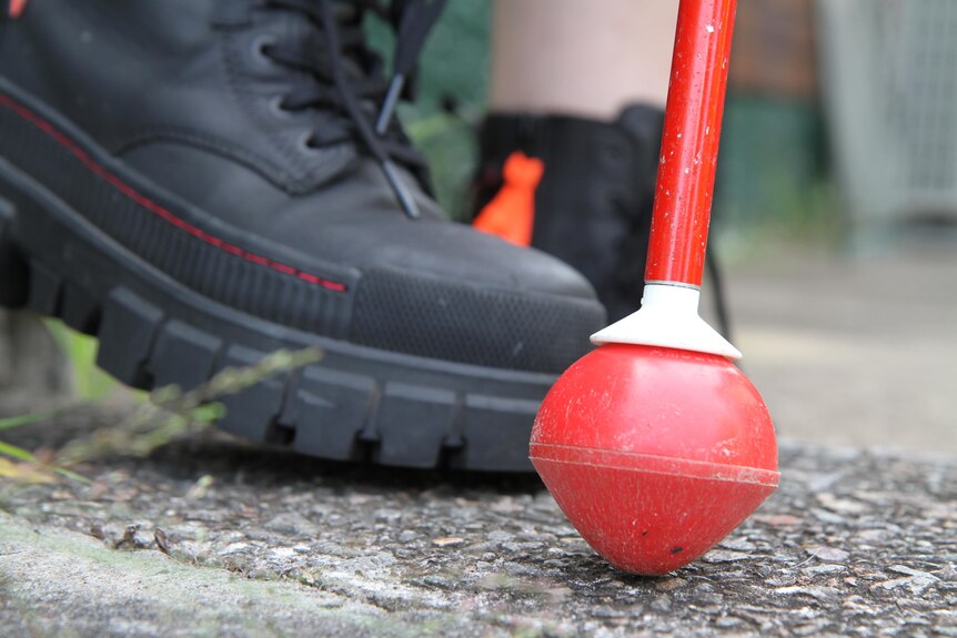 A close-up of Nicola's black boots walking on the path, with a bright red cane.