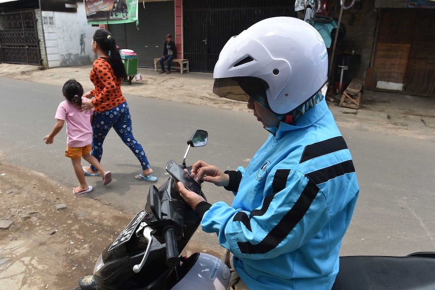 A female motorcycle taxi driver checks her smartphone in Jakarta