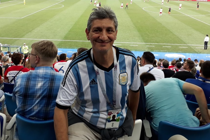A man wearing an Argentina jersey stands in the stands of a football game.