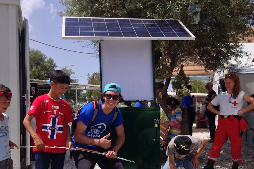 Migrants and Elpis team stand next to sun-powered phone charging station