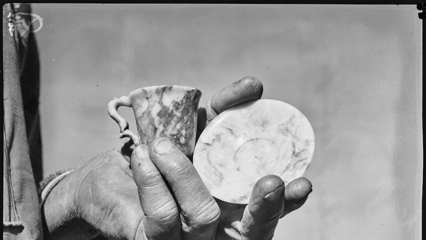 Hand holding a teacup and saucer carved from marble.