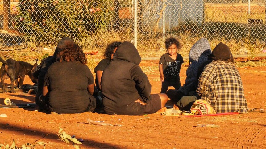 A group of people sit around on the ground talking.
