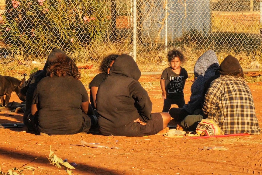 A group of people sit around on the ground talking.