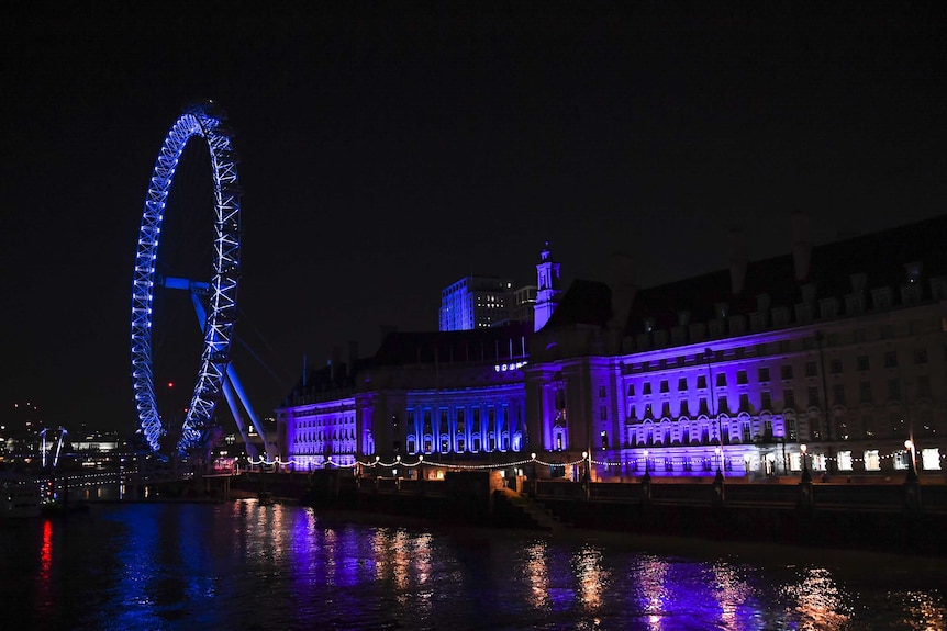 The London Eye is lit up with blue as well as other buildings along the Thames.