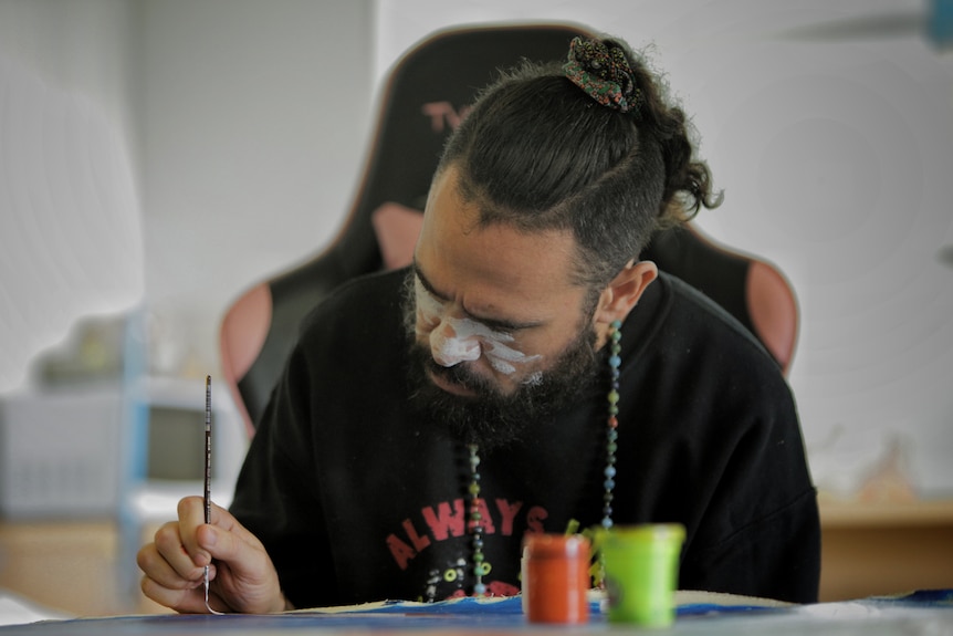 Aboriginal man wearing a black shirt painting. 