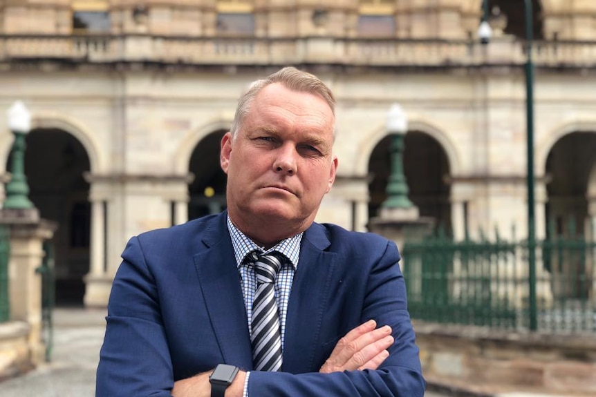 A man in front of stately buildings with his arms crossed.