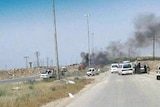 Black smoke rises ahead of cars stopped on a road into the Syrian city known as Castello Road.