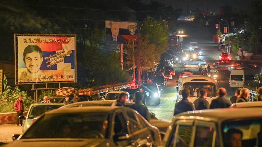 A well-lit street filled with cars and people at night.