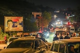 A well-lit street filled with cars and people at night.