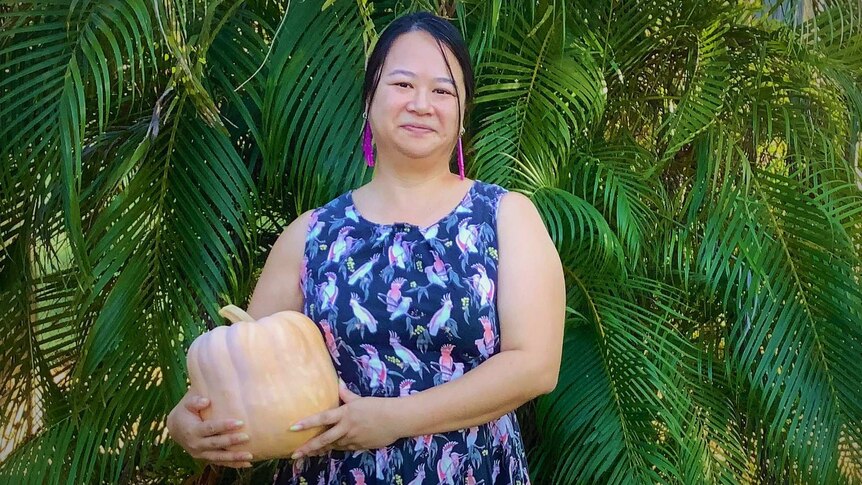 Woman standing before palm trees holding a pumpkin