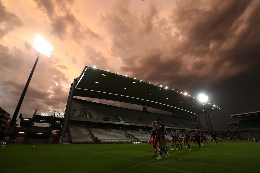 Soccer players walk in a line along the grass with a sunset and clouds in the background