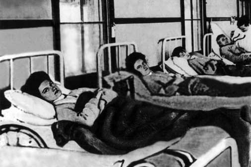 A row of women lying in beds in a hospital dorm