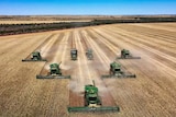 Five green harvesters working in a paddock. 