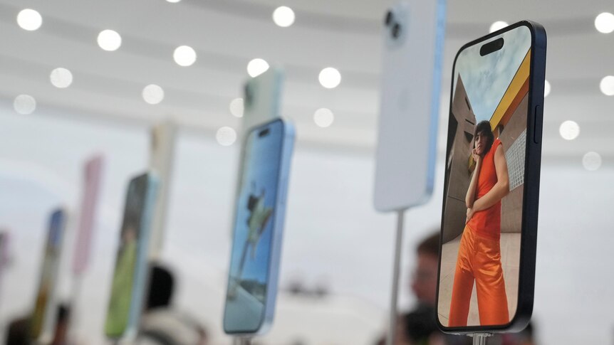 Apple iPhone 15s sit on stands in a brightly lit showroom