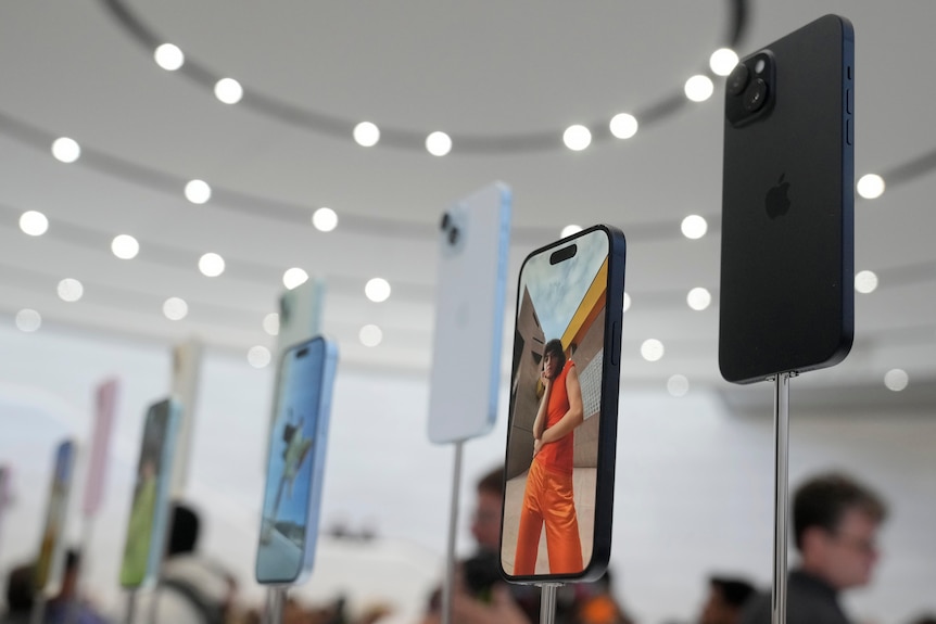 Apple iPhone 15s sit on stands in a brightly lit showroom