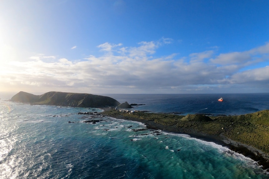 View over a green island in a blue ocean with an orange ship to the left